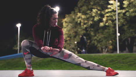 Sportive-Curly-Girl-Training-And-Stretching-Legs-In-The-Park-At-Night-1