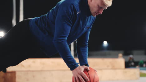 Sportive-Blond-Man-Doing-Push-Ups-Using-Basketball-In-The-Park-At-Night