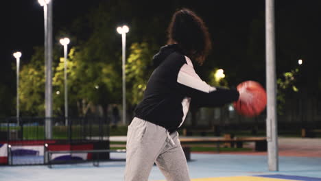 Konzentriertes-Weibliches-Basketballspielertraining-Mit-Ball-Nachts-Auf-Dem-Außenplatz