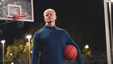 Portrait-Of-A-Confident-Basketball-Player-Holding-Ball-And-Looking-At-Camera-While-Standing-On-An-Outdoor-Court-At-Night
