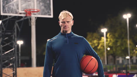 Portrait-Of-A-Confident-Basketball-Player-Holding-Ball-And-Looking-At-Camera-While-Standing-On-An-Outdoor-Court-At-Night-1