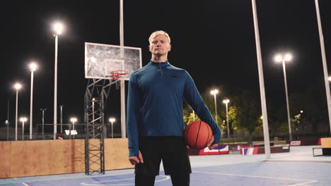 Confident-Basketball-Player-Holding-Ball-And-Looking-At-Camera-While-Standing-On-An-Outdoor-Court-At-Night-1