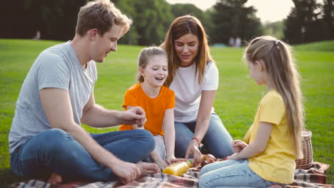 Glückliche-Eltern-Mit-Zwei-Kleinen-Töchtern,-Die-Zusammen-Picknicken-Auf-Der-Grünen-Wiese-Im-Park