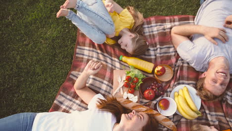 Top-View-Of-Happy-Family-Lying-On-Blanket-In-Park,-Laughing-And-Having-Fun-Together-While-Having-A-Picnic-In-The-Park