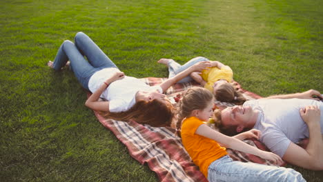Happy-Family-Lying-On-Blanket-In-Park,-Laughing-And-Having-Fun-Together-While-Having-A-Picnic-In-The-Park