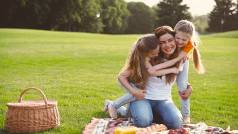 Two-Cute-Little-Sisters-Running-And-Embracing-Her-Happy-Mother-From-Back-At-Park-During-Picnic