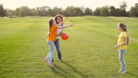 Glückliche-Mutter-Und-Ihre-Zwei-Kleinen-Töchter-Spielen-Mit-Ball-Auf-Der-Wiese