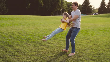 Happy-Father-Holding-Her-Little-Daughter-And-Spinning-Around-On-Green-Grass-In-The-Park