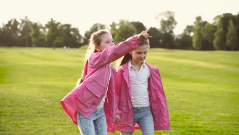 Two-Happy-Little-Sisters-In-Identical-Clothes-Holding-Hands-And-Walking-Together-In-The-Park