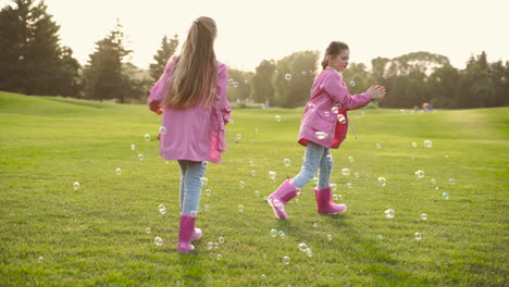 Glückliche-Kleine-Schwestern-In-Identischer-Kleidung,-Die-Im-Park-Seifenblasen-Fangen