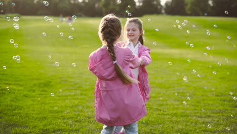 Happy-Little-Sisters-In-Identical-Clothes-Surronding-By-Soap-Bubbles-Holding-Hands-And-Spinning-Around-In-The-Park