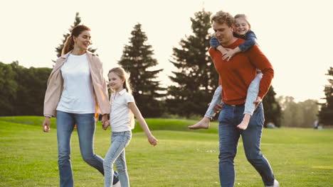Glückliche-Eltern-Mit-Ihren-Zwei-Kleinen-Mädchen,-Die-Zusammen-Im-Park-Spazieren-Gehen