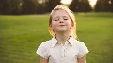 Portrait-Of-A-Cute-Blonde-Little-Girl-With-Closed-Eyes-Smiling-Surronded-By-Soap-Bubbles-In-The-Park