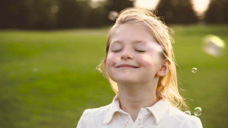Portrait-Of-A-Cute-Blonde-Little-Girl-With-Closed-Eyes-Laughing-Surronded-By-Soap-Bubbles-In-The-Park