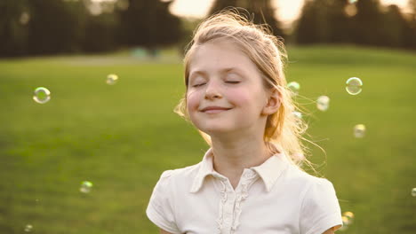 Portrait-Of-A-Cute-Blonde-Little-Girl-With-Closed-Eyes-Smiling-Surronded-By-Soap-Bubbles-In-The-Park-3