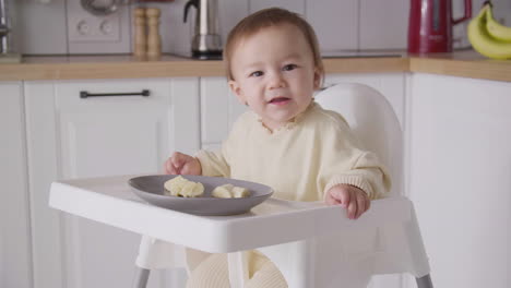 Süßes-Kleines-Mädchen,-Das-Bananenscheiben-Isst-Und-In-Ihrem-Hochstuhl-In-Der-Küche-Sitzt
