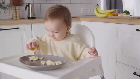 Süßes-Kleines-Mädchen,-Das-Bananenscheiben-Isst-Und-In-Ihrem-Hochstuhl-In-Der-Küche-Sitzt-7