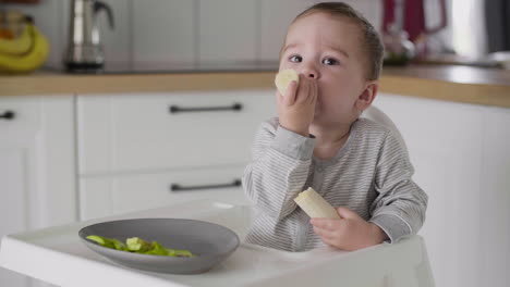 Cute-Baby-Boy-Eating-Banana-Sitting-In-High-Chair-In-The-Kitchen-1