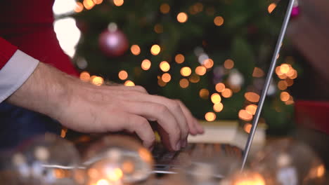 Nahaufnahme-Von-Mannhänden,-Die-Auf-Einem-Laptop-Tippen,-Der-In-Der-Nähe-Des-Weihnachtsbaums-Im-Wohnzimmer-Mit-Weihnachtsdekoration-Sitzt-1