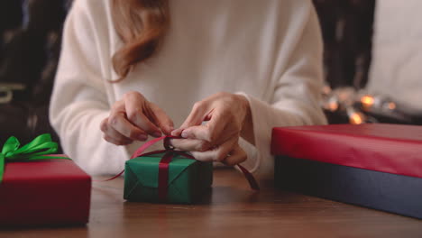 Close-Up-View-Of-Woman-Hands-Wrapping-A-Christmas-Present-With-A-Bow-On-A-Table