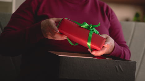Close-Up-View-Of-A-Woman's-Hands-Taking-Out-Christmas-Gift-From-A-Box-Sitting-On-The-Sofa