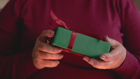 Close-Up-View-Of-A-Woman's-Hands-Holding-Christmas-Gift-From-A-Box-Sitting-On-The-Sofa
