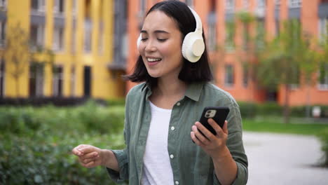 Happy-Young-Japanese-Girl-Enjoying-Music-In-Wireless-Headphones-While-Walking-And-Dancing-In-The-Street