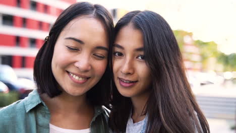 Outdoor-Portrait-Of-Two-Beautiful-Young-Japanese-Girls-Looking-And-Smiling-At-Camera