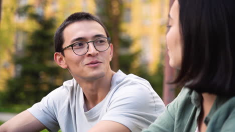 Young-Japanese-Man-Talking-And-Laughing-With-His-Female-Friend-While-Sitting-Together-Outdoors