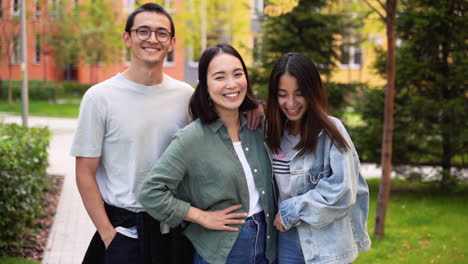 Group-Of-Three-Young-Japanese-Friends-Smiling-And-Looking-At-Camera-While-Standing-Outdoors-1