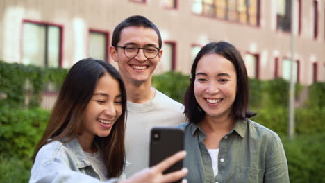 Group-Of-Three-Young-Japanese-Friends-Standing-Outdoors,-Taking-Funny-Selfie-Photos-And-Laughing-Together