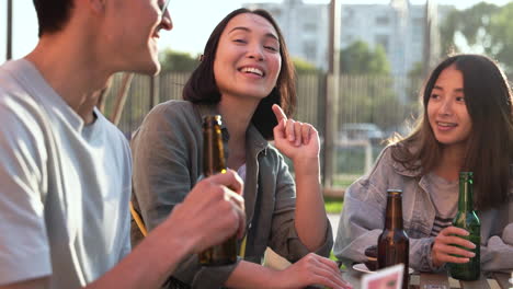 Gruppe-Von-Drei-Japanischen-Freunden,-Die-An-Einem-Sonnigen-Tag-Im-Freien-Am-Tisch-Sitzen-Und-Bier-Reden-Und-Trinken