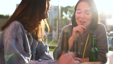 Group-Of-Three-Japanese-Friends-Talking-And-Holding-Beers-While-Sitting-At-Table-Outdoors-In-A-Sunny-Day