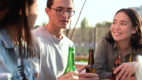 Grupo-De-Tres-Amigos-Japoneses-Hablando-Y-Bebiendo-Cerveza-Mientras-Se-Sientan-En-La-Mesa-Al-Aire-Libre-En-Un-Día-Soleado-1