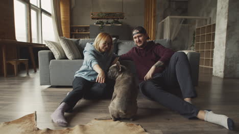 Couple-Sitting-On-The-Floor-Leaning-On-The-Sofa-Caressing-Their-Bulldog-Dog-2