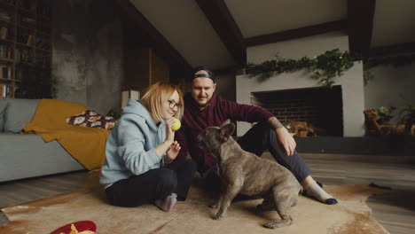 Couple-Playing-With-Her-Bulldog-Dog-With-A-Tennis-Ball-On-The-Floor-In-Living-Room-2