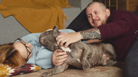 Couple-Caressing-Her-Bulldog-Dog-Liying-On-The-Floor-In-Living-Room