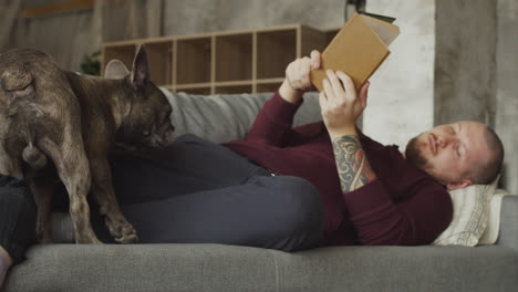 Man-Lying-On-The-Sofa-With-His-Bulldog-Dog-While-Reading-A-Book