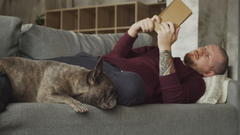 Man-Lying-On-The-Sofa-With-His-Bulldog-Dog-While-Reading-A-Book-1