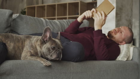 Man-Lying-On-The-Sofa-With-His-Bulldog-Dog-While-Reading-A-Book-2