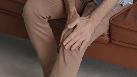 Close-Up-Of-An-Unrecognizable-Man-Having-A-Knee-Pain-While-Sitting-On-Sofa-At-Home
