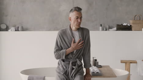 Leidender-Mann-In-Pyjama-Und-Robe,-Der-Brustschmerzen-Hat-Und-Seinen-Herzbereich-Im-Badezimmer-Zu-Hause-Berührt