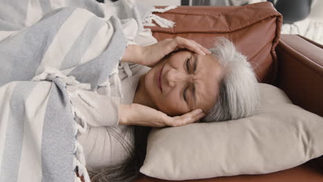 Kranke-Frau-Mittleren-Alters,-Die-Kopfschmerzen-Hat,-Während-Sie-Auf-Der-Mit-Einer-Decke-Bedeckten-Couch-Liegt