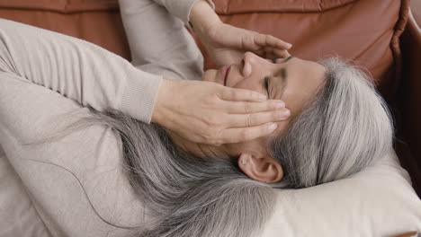 Kranke-Frau-Mittleren-Alters,-Die-Kopfschmerzen-Hat,-Während-Sie-Zu-Hause-Auf-Der-Couch-Liegt