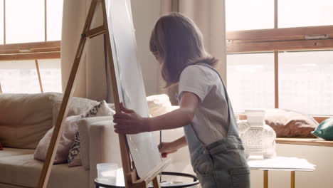 Side-View-Of-A-Blonde-Girl-Painting-Her-Drawing-With-A-Brush-On-A-Lectern-In-The-Living-Room-At-Home