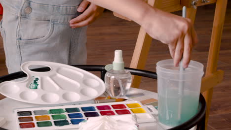 Close-Up-View-Of-A-Girl's-Hands-Wetting-The-Brush-With-Water-And-Mixing-It-With-Green-Paint