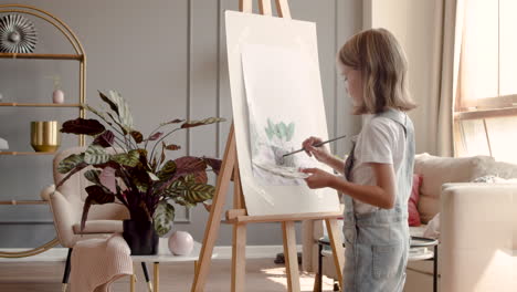 Rear-View-Of-A-Blonde-Girl-Painting-A-Plant-With-A-Brush-On-A-Lectern-In-The-Living-Room-At-Home-3