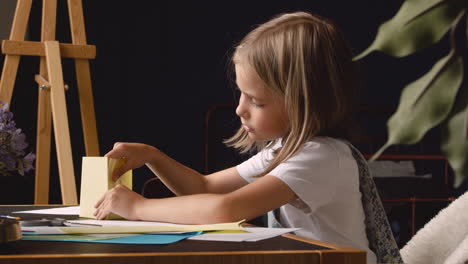 Side-View-Of-Blonde-Girl-Building-Geometrics-Shapes-With-Cardboard-Sitting-At-Desk