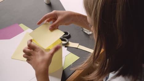 Top-View-Of-Blonde-Girl-Cutting-Cardboard-And-Building-Geometric-Shape-Sitting-At-Desk
