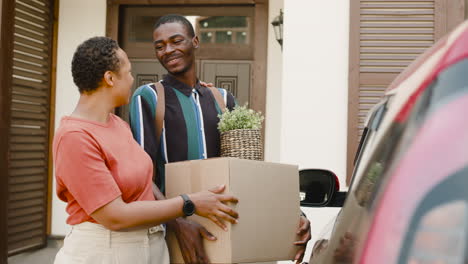 Young-Man-Holding-Box-Walking-With-His-Mom-Towards-Car-Before-Moving-Home